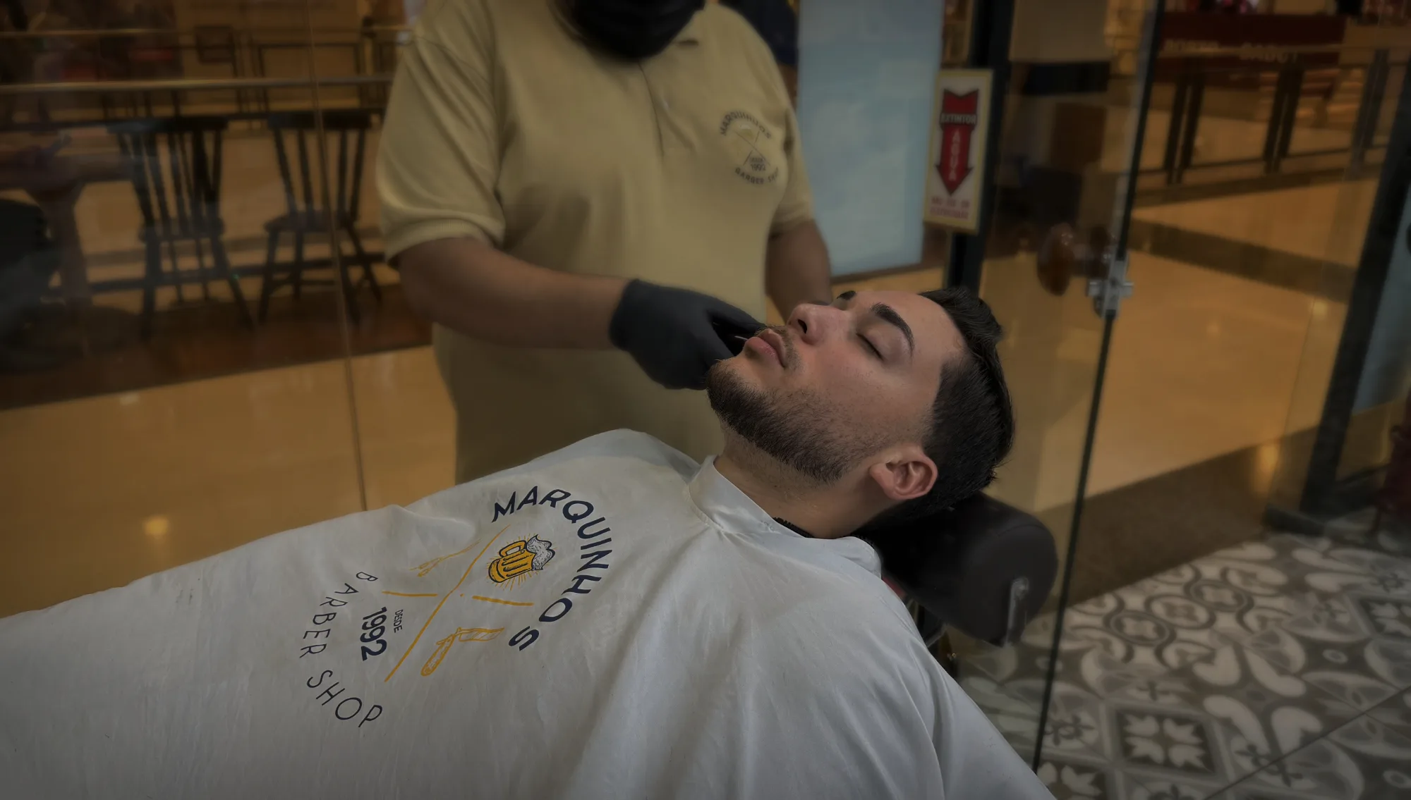 Barbeiro aparando a barba de um cliente numa unidade da Marquinhos Barber Shop