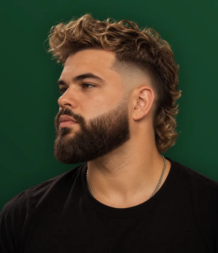 Homem de perfil com mullet ondulado e barba cheia